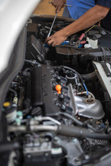 Car service by an auto mechanic in garage, fixing a car battery with wrench, also checking some parts of the engine showing by selective focus.