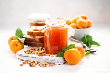 Apricot jam in a jar and fresh fruits with nuts on  wooden cutting board. Healthy breakfast