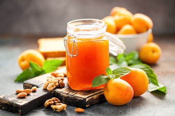 Apricot jam in a jar and fresh fruits with nuts on  wooden cutting board. Healthy breakfast