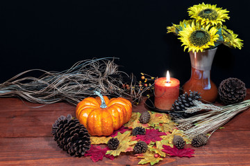 Silk maple leaves, beautiful bouquet of sunflowers, frosted pinecones and orange candle on tabletop with dark background.