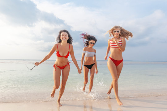 Three beautiful slender happy girlfriends having fun on the beach rejoicing and having fun against the background of the sea, vacation time and travel