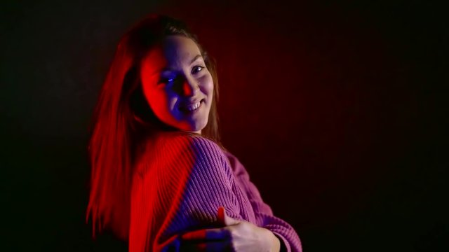 cheerful girl is rejoicing in dark studio with red, blue and white lights, hugging herself