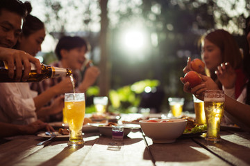 Asian group eating and drinking cold beer outside the house at night, having fun talking