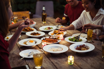 Asian group eating and drinking cold beer outside the house at night, having fun talking