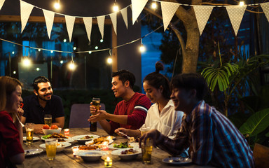 Asian group eating and drinking cold beer outside the house at night, having fun talking