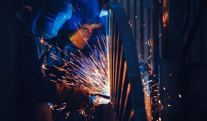 Professional welder performs welding work on metal in protective mask. Industrial worker concept - obrazy, fototapety, plakaty