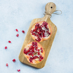 Two half pomegranate fruit lay on wooden board on blue table background. Top view, copy space