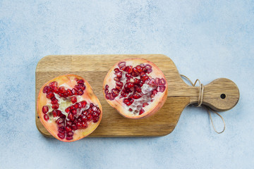 Two half pomegranate fruit lay on wooden board on blue table background. Top view, copy space