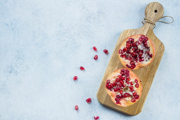 Two half pomegranate fruit lay on wooden board on blue table background. Top view, copy space