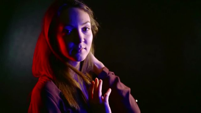 young pretty woman is posing in dark studio, medium shot, red blue white lights are on her face