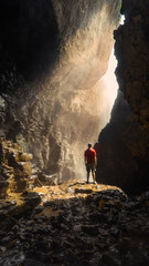 Obraz premium Male Backpacker wearing a red shirt standing in sunlight in a cave beneath the Elephant waterfall in Dalat Vietnam.