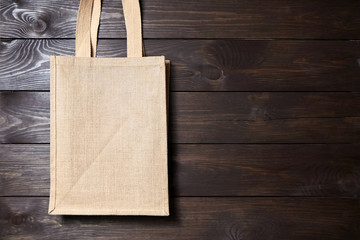 Reusable shopping bag, natural textile fiber, blank eco hessian or jute sack on brown wooden background