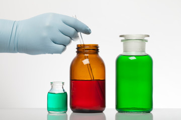 A hand in laboratory gloves mixes chemistry. Liquid in laboratory bottles. Scientific biochemical laboratory. Colorful liquid.