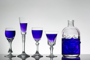 A skull bottle and crystal glasses with a liquid, alcohol drink.
