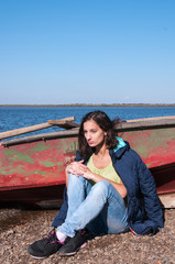 Brunette girl in a jacket in the fall near a boat on the bank of the Amur River, below the village of Sikachi-Alyan
