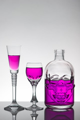 A skull bottle and crystal glasses with a liquid, alcohol drink.