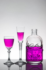 A skull bottle and crystal glasses with a liquid, alcohol drink.