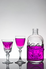 A skull bottle and crystal glasses with a liquid, alcohol drink.