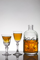 A skull bottle and crystal glasses with a liquid, alcohol drink.