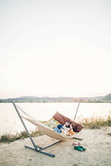 Fototapeta na wymiar happy hipster couple with bulldog relaxing in hammock on the beach in sunset light, summer vacation. stylish family with dog cuddling and resting, cute moments. space for text.