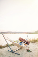 Fototapeta na wymiar happy hipster couple with bulldog relaxing in hammock on the beach in sunset light, summer vacation. stylish family with dog cuddling and having fun, cute moments in summer evening