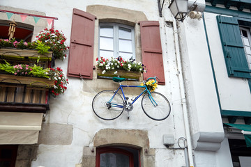 Fototapeta na wymiar Bicycle is hanging under the window with wooden shutters on the wall of the facade of the building. Traditional red and white basque house