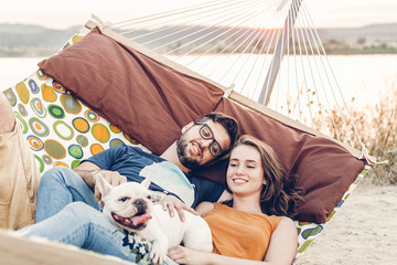Hipster couple on a trip to the beach, young freelancer man relaxing in a hammock with his woman,...