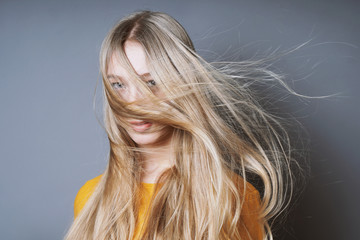 blond young woman with long windswept tousled hair blowing into her face