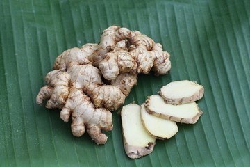 Fresh ginger root and ginger sliced on green leaf background on wood table background, tropical...