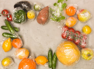 many different fruits and vegetables are wrapped in plastic foil, packed on concrete background