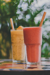 Zwei gesunde Smoothies stehen vor Palmenblättern