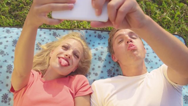 SLOW MOTION, CLOSE UP: Goofy couple making funny faces while taking selfies for their social media. Beautiful woman and handsome man sticking out their tongue and making faces as they take photos.