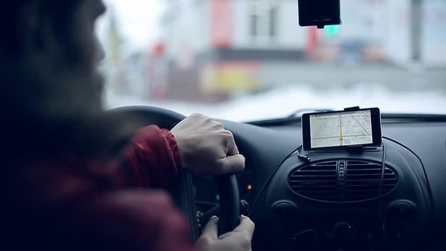 A man gets into the car and turns on the navigator on the smartphone
