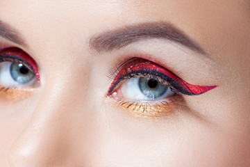 Obraz premium Amazing Bright eye makeup in luxurious red arrow. Red and gold shining tones, eye shadow.