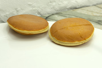 Sweet pancakes on plate with condensed milk on table