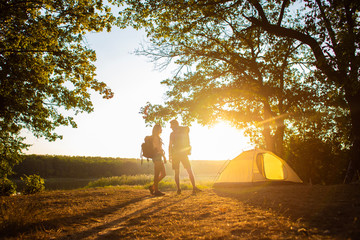 A man and a woman in a hiking trip with backpacks near a tent at sunset. Honeymoon in nature