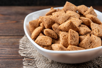 Dried breakfast pads in white bowl on dark wooden background.