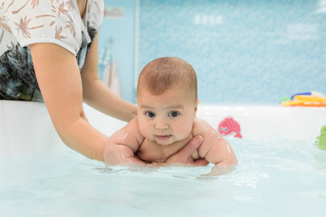 Fototapeta na wymiar Cute baby swimming in bathroom. The instructor teaches mom infants fitness and swimming