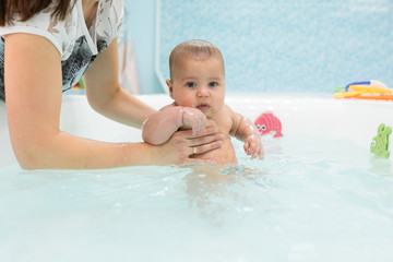 Fototapeta na wymiar Cute baby swimming in bathroom. The instructor teaches mom infants fitness and swimming