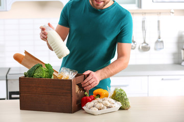 Man with wooden crate full of products at table in kitchen. Food delivery service