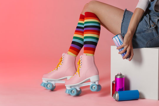 Woman with vintage roller skates and spray paint cans on color background, closeup. Space for text