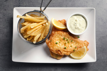 Plate with British traditional fish and potato chips on grey table, top view