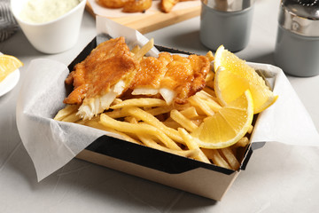 Container with British traditional fish and potato chips on table