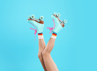 Young woman with retro roller skates on color background, closeup