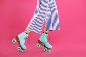 Young woman with retro roller skates on color background, closeup