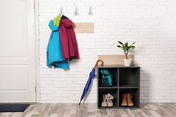 Stylish hallway interior with shoe rack and hanging clothes on brick wall