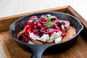 Breakfast in a pan on a white background. Pancakes with cream and jam. On a wooden tray.