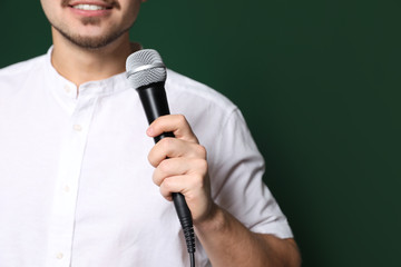Young man in casual clothes holding microphone on color background, closeup with space for text