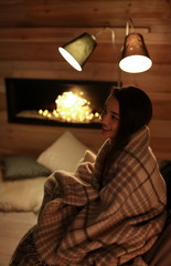 Young woman resting near decorative fireplace at home. Winter season