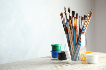Glass with brushes and paint jars on table against light background. Space for text
